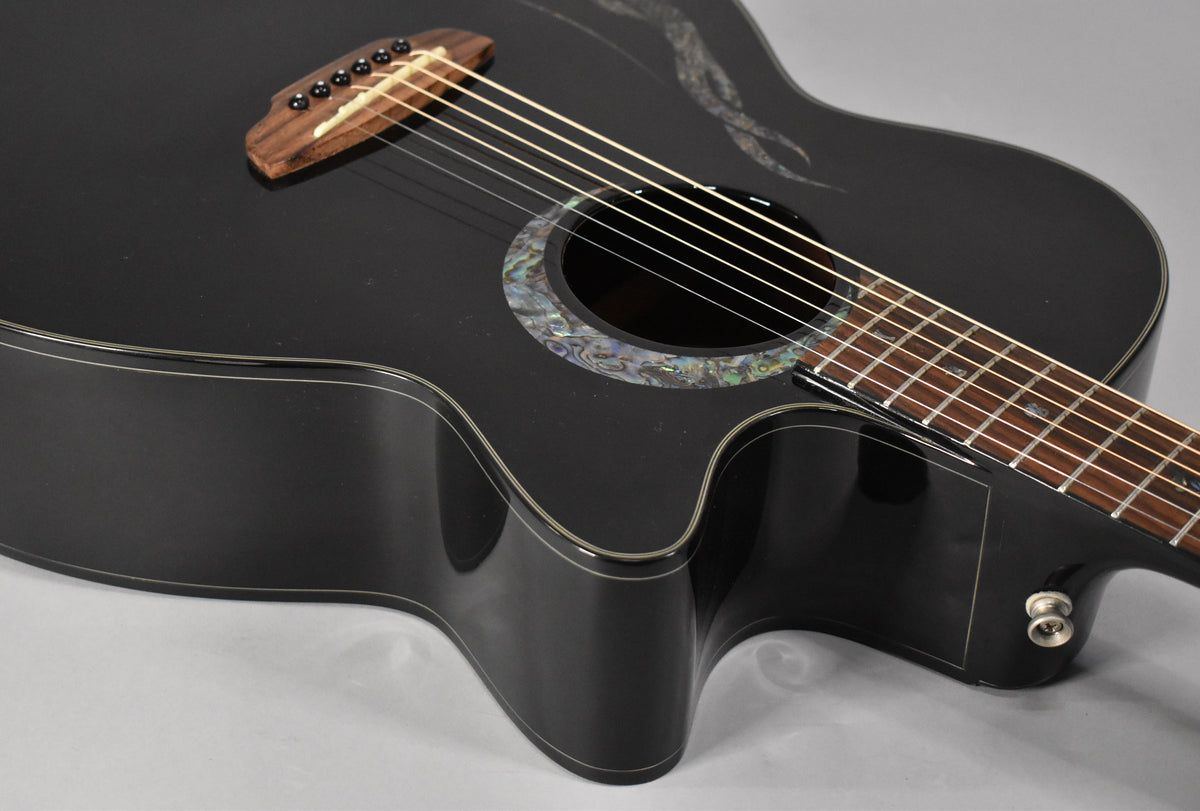 Close-up of the black acoustic guitar's body, showing the abalone rosette, wooden bridge, and cutaway with an output jack.