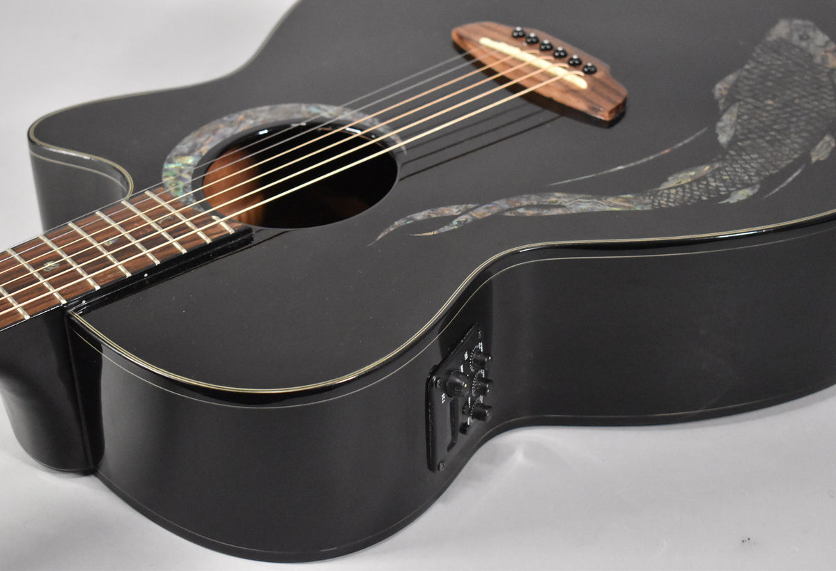 The black acoustic guitar's upper bout and cutaway show a mother-of-pearl koi inlay and an onboard preamp with three knobs.