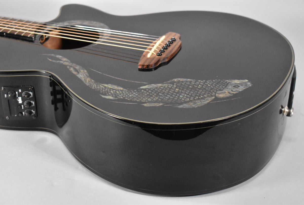 A close-up of the glossy black guitar body, angled from the lower bout, showing the koi inlay, bridge, and preamp controls.