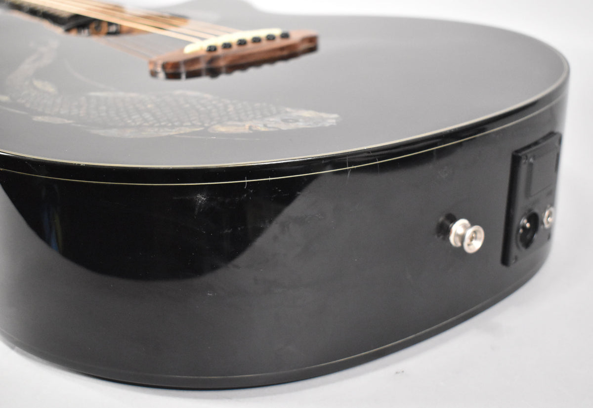 The black acoustic guitar's lower bout shows a 1/4" jack, XLR output, and light scratches on its glossy finish.