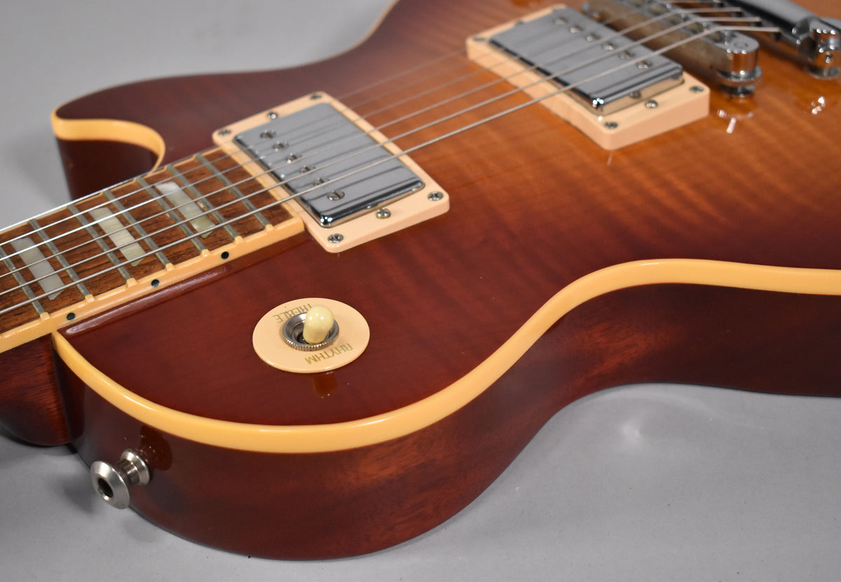 Close-up of the cherry sunburst body, showing the rhythm/treble switch, output jack, and neck binding with trapezoid inlays.