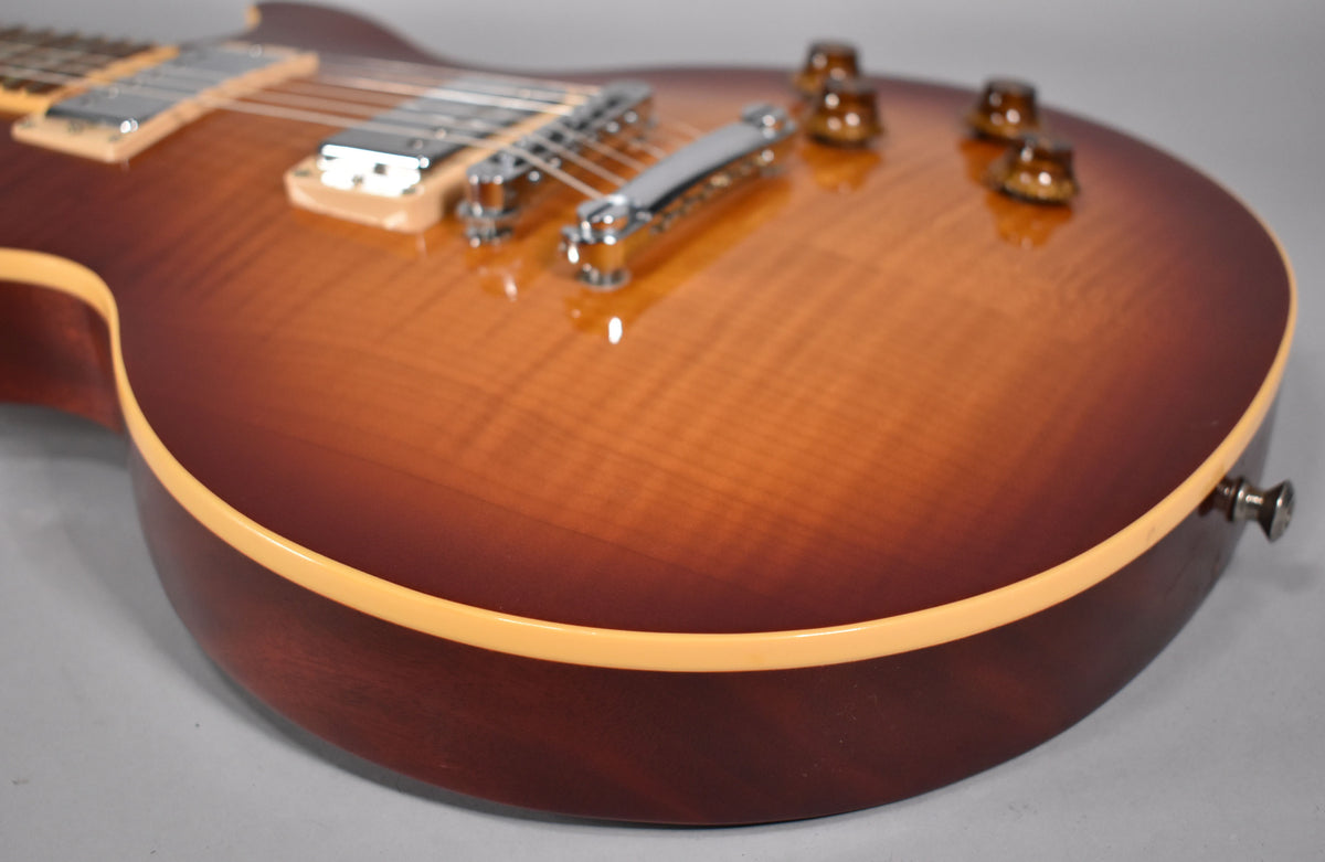 The guitar's cherry sunburst body, with visible wood grain, is angled to show the chrome bridge, tailpiece, and four amber control knobs.