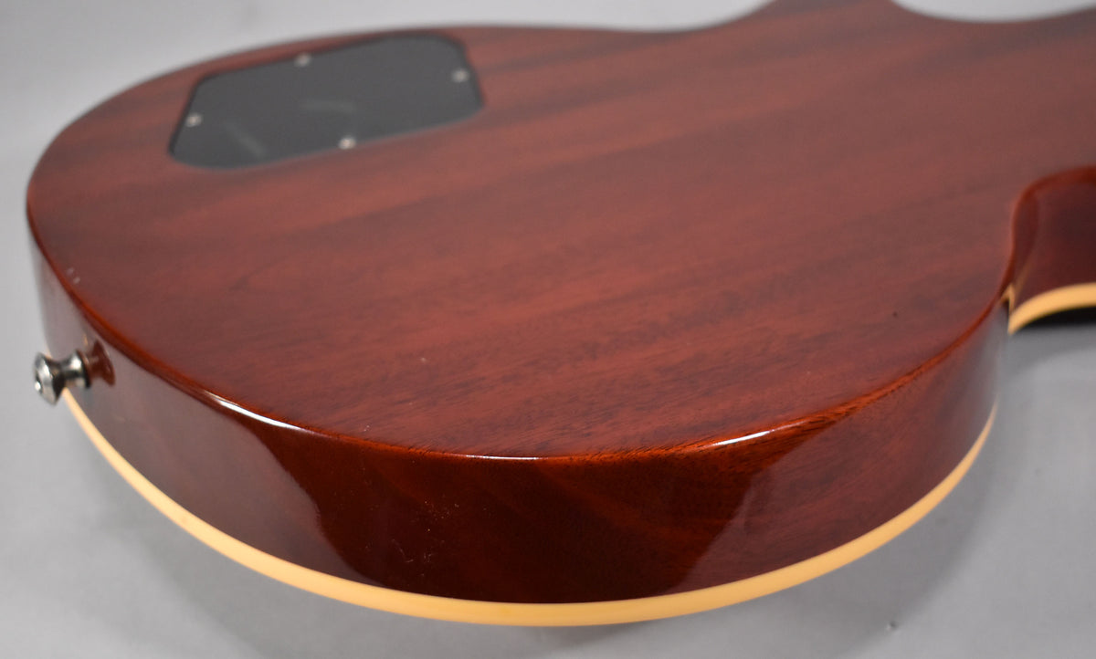 The back of the cherry sunburst guitar body, showing the control cavity cover, strap button, and cream binding along the edge.