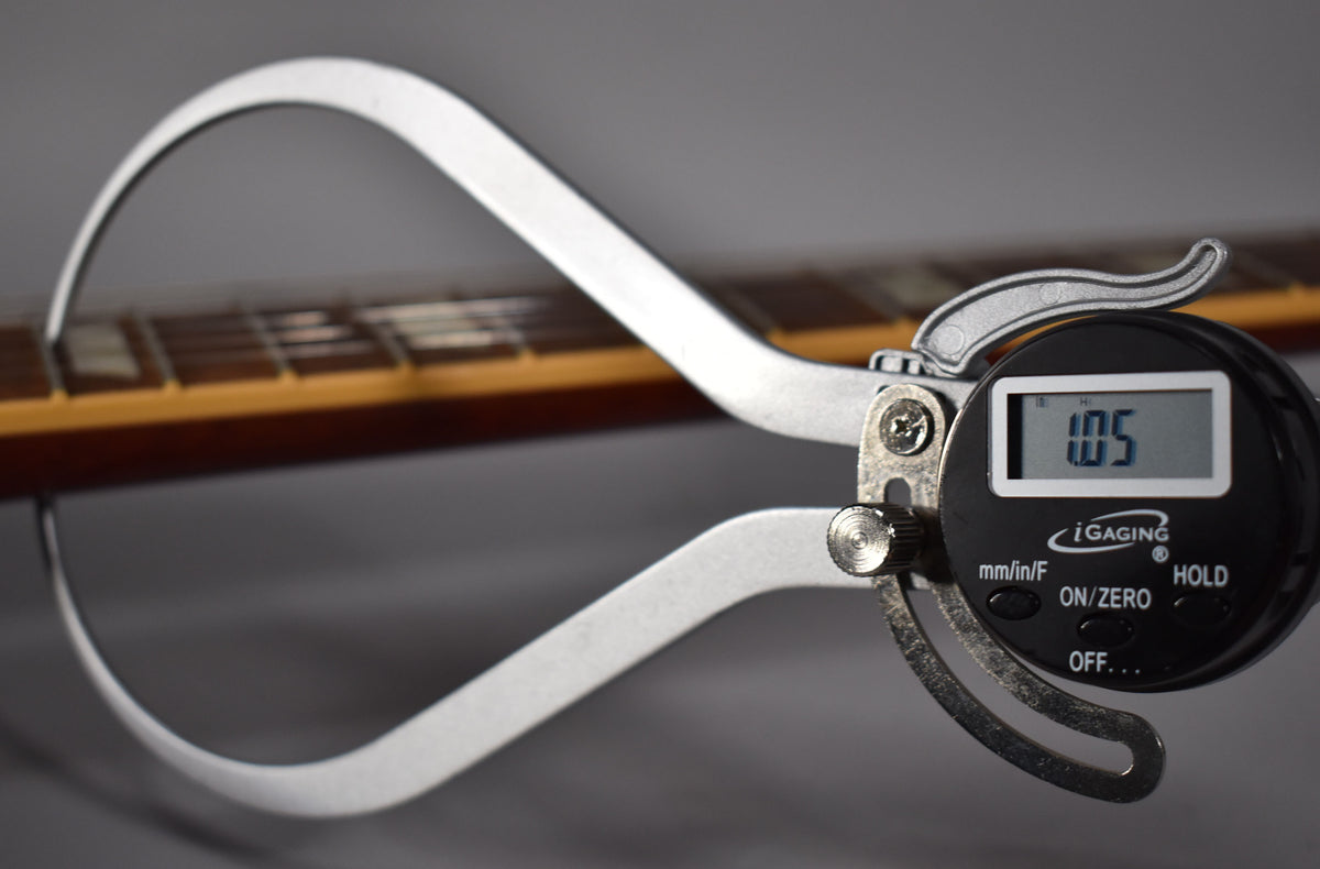 A digital caliper measures the guitar's fretboard, showing a reading of 1.05, with the frets and neck visible in the background.