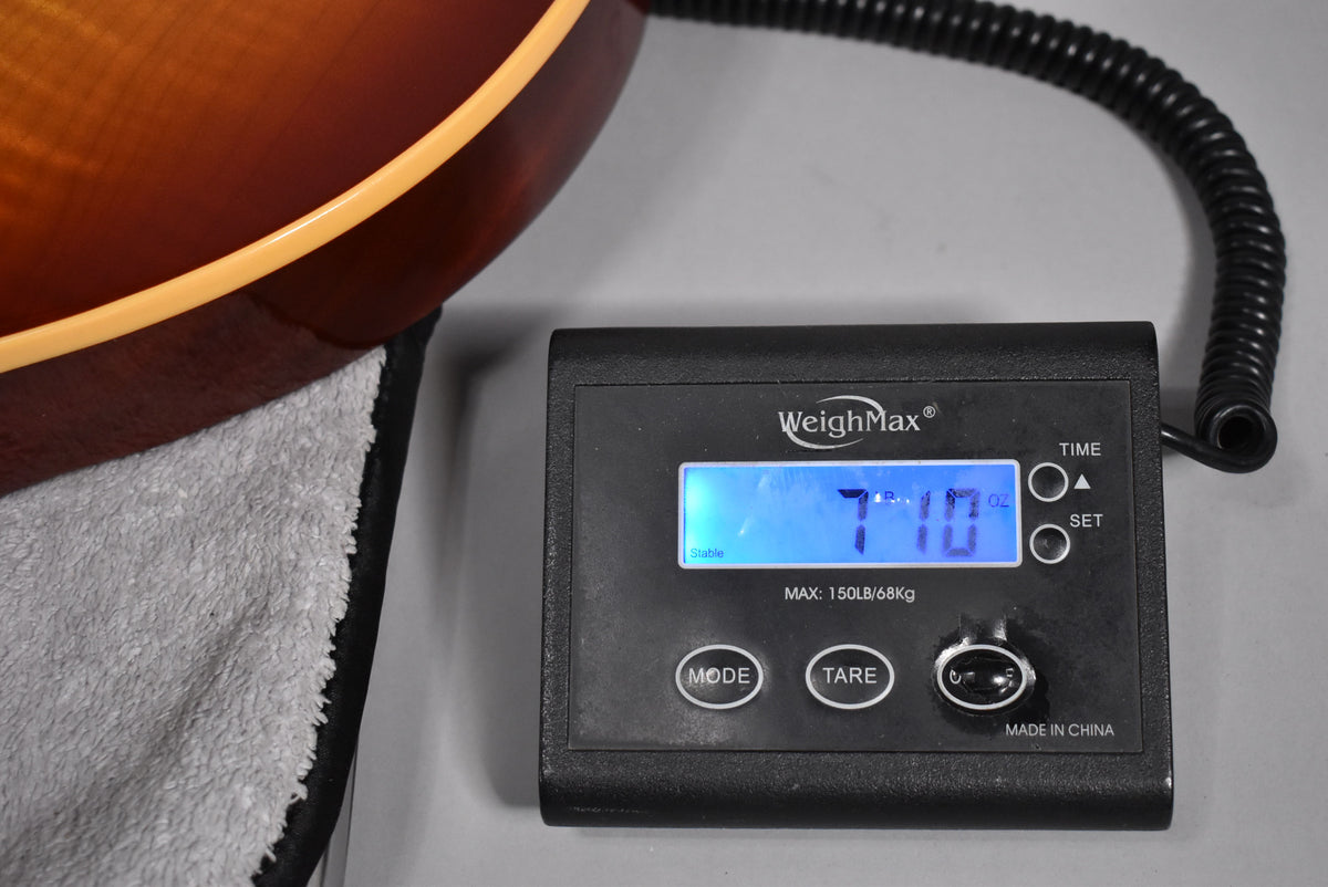 The guitar's cherry sunburst body is partially visible on a scale displaying 7lb 10oz, resting on a gray towel.