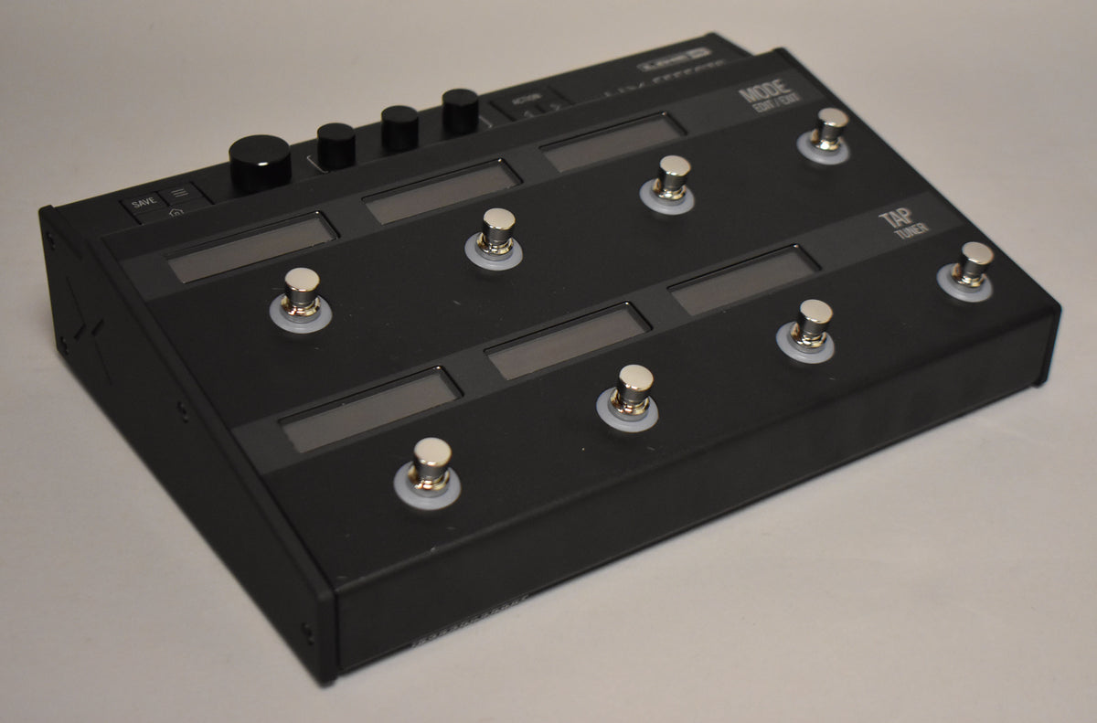 A black multi-effects pedal is angled from the left, showing its top panel with six footswitches, six screens, and four control knobs.