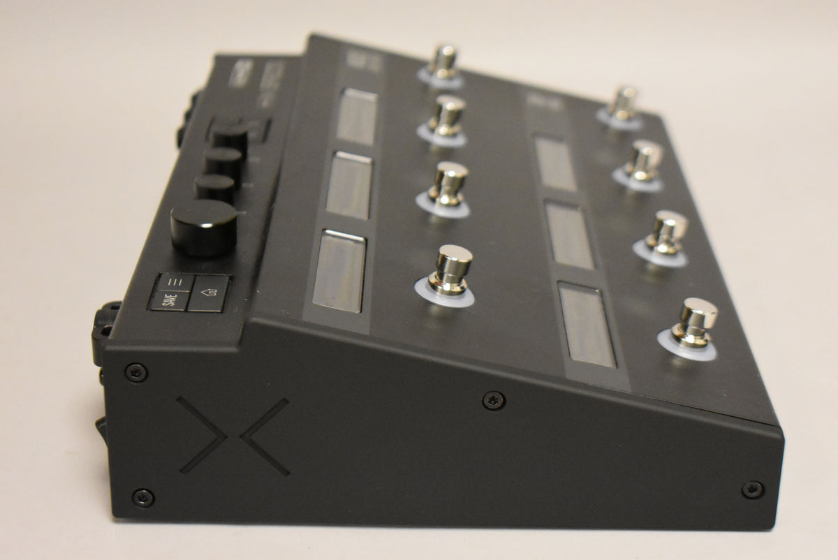 A black multi-effects pedal is angled right, showing its top panel with 10 silver footswitches, 6 screens, and 4 black control knobs.