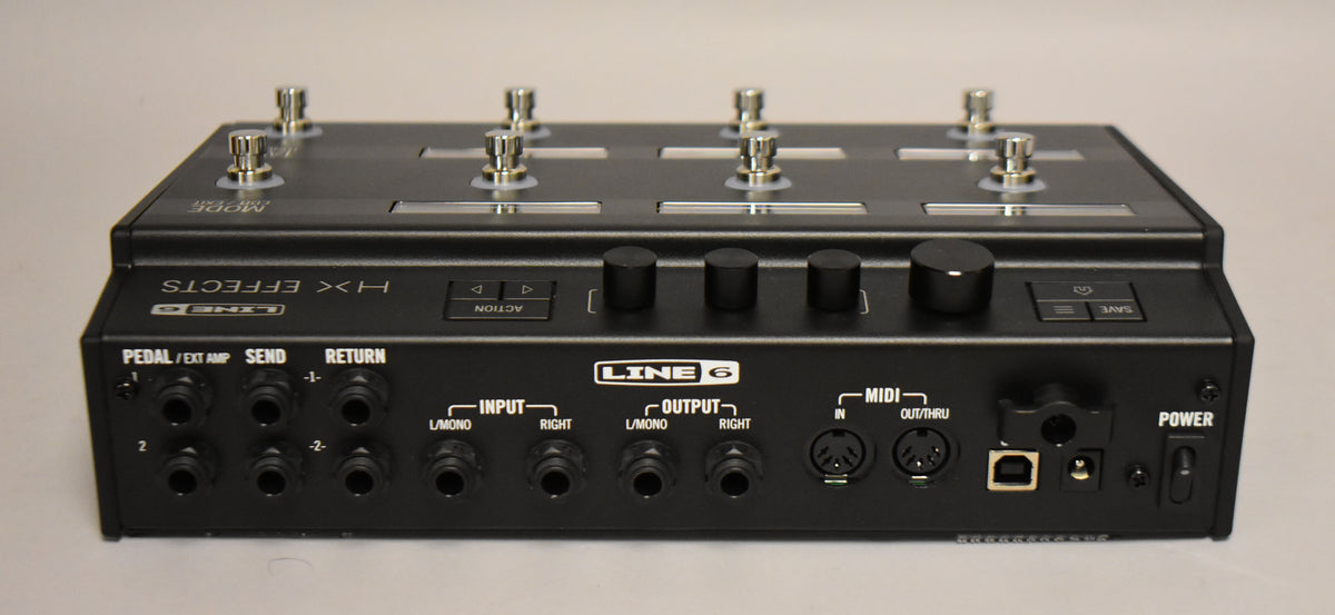 The black multi-effects pedal is seen from the rear, showing its many input/output jacks, MIDI ports, USB port, and power switch.