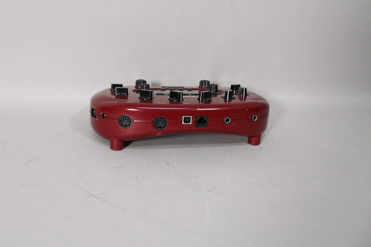 The dark red, rounded pedal is viewed from the rear, showing two MIDI ports, a USB port, an ethernet port, and two audio jacks.