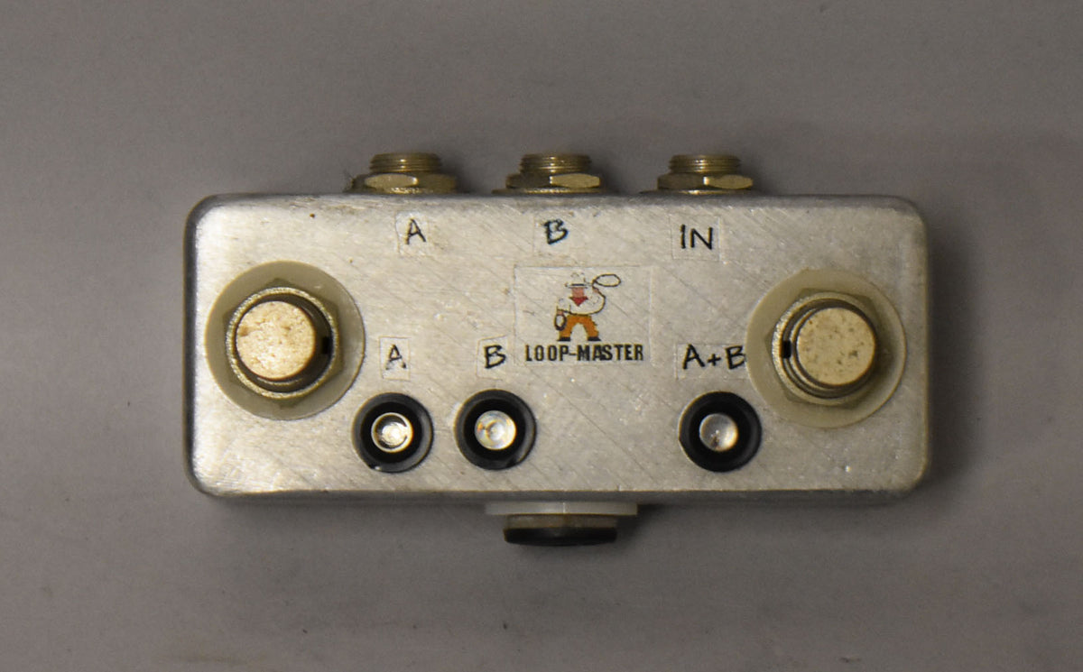 Top-down view of a brushed aluminum pedal with three brass jacks, two large cream footswitches, and three smaller black LED indicators.