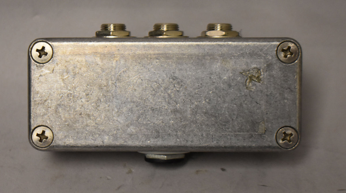 The Loop-Master ABY Box is a rectangular, brushed aluminum pedal with three brass jacks on top and four visible corner screws.