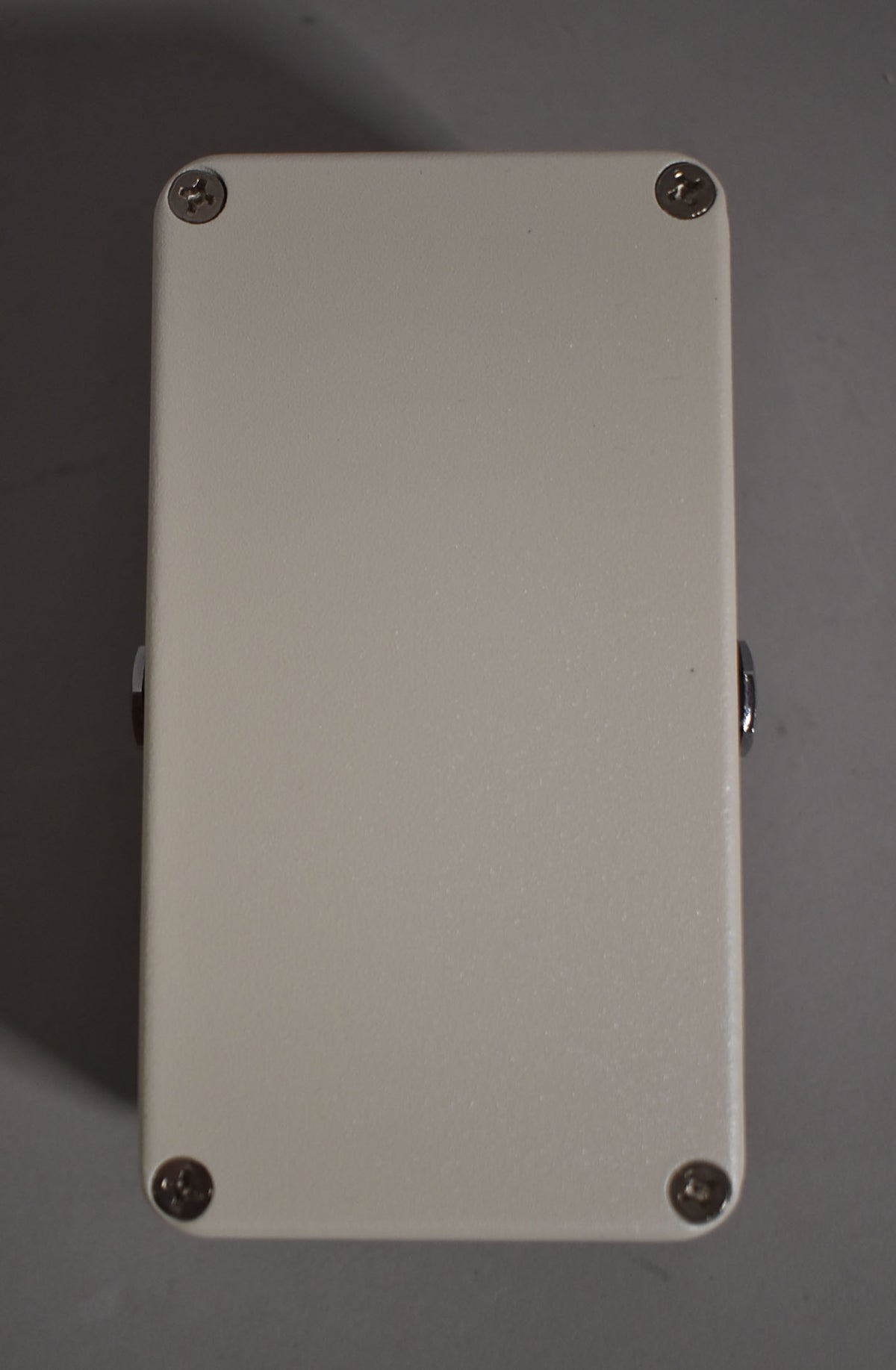 The pedal's off-white textured bottom plate is visible, secured by four silver Phillips head screws at each corner.