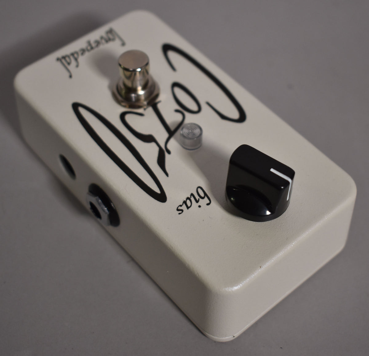 Cream-colored guitar pedal, angled from the left, showing a chrome footswitch, a clear LED, and a black control knob.