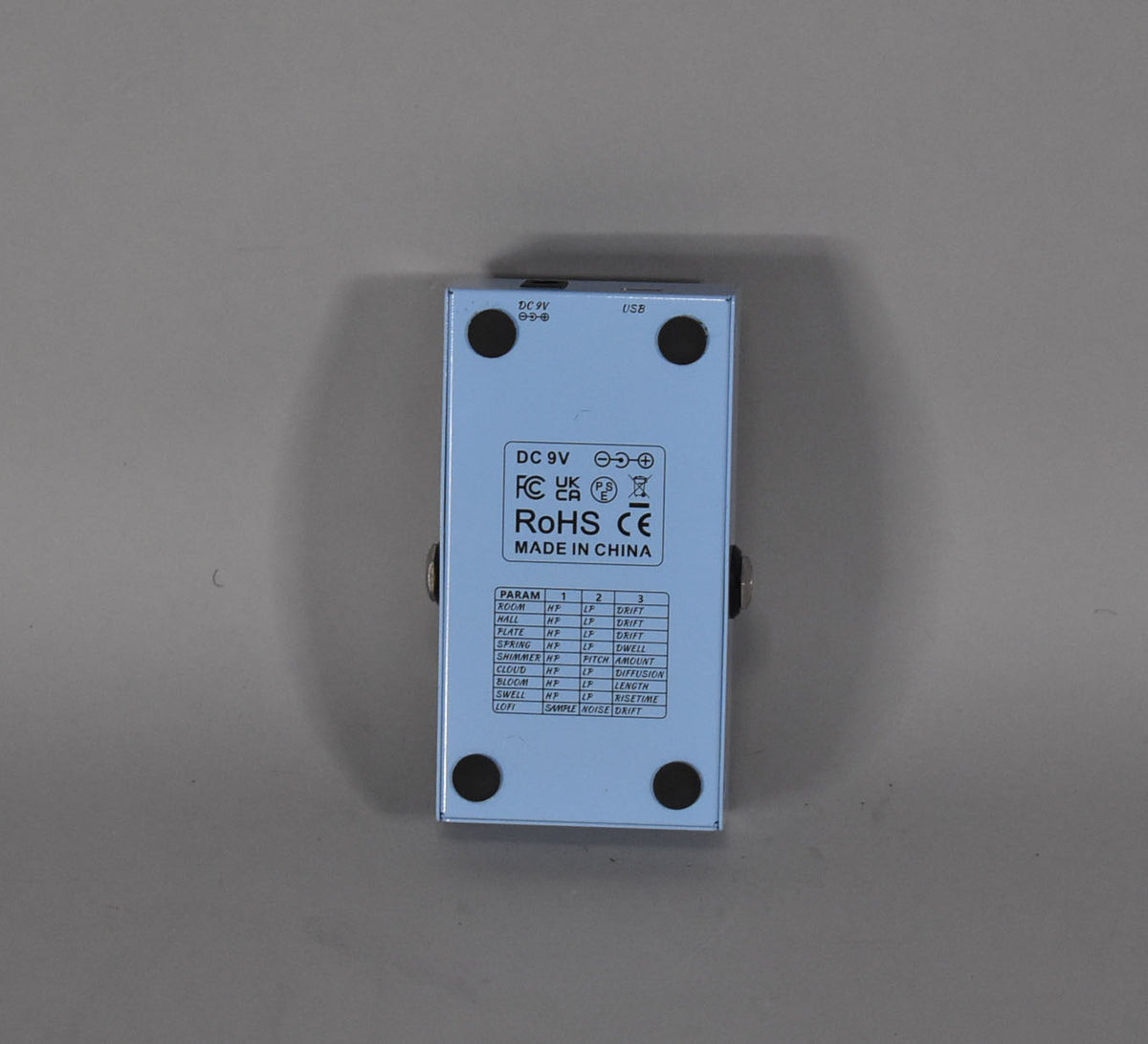 The light blue pedal is seen from the back, showing the DC 9V and USB inputs, and a table of reverb parameters.