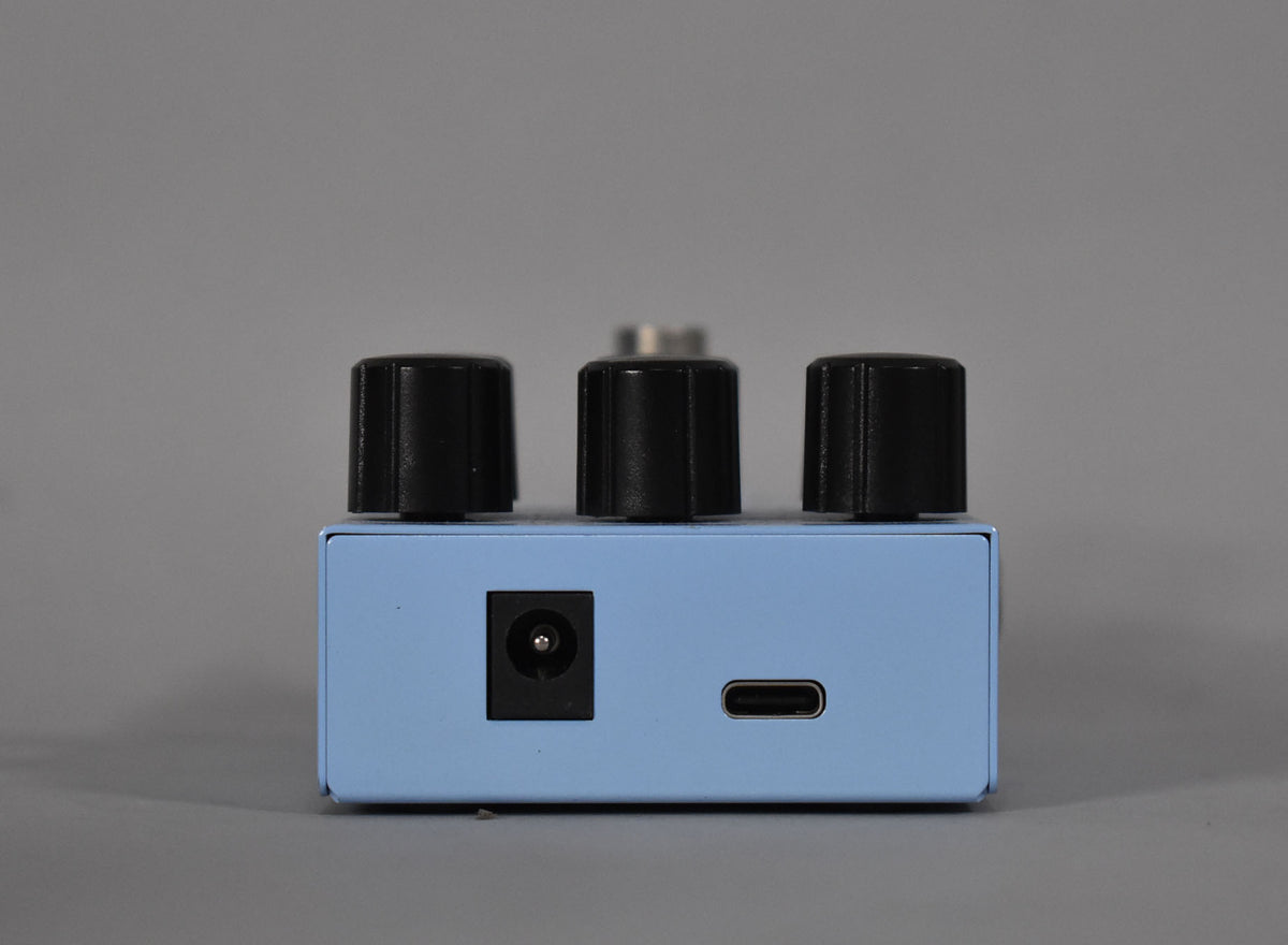 The light blue pedal's rear shows a DC power input and a USB-C port, with three black control knobs visible above.