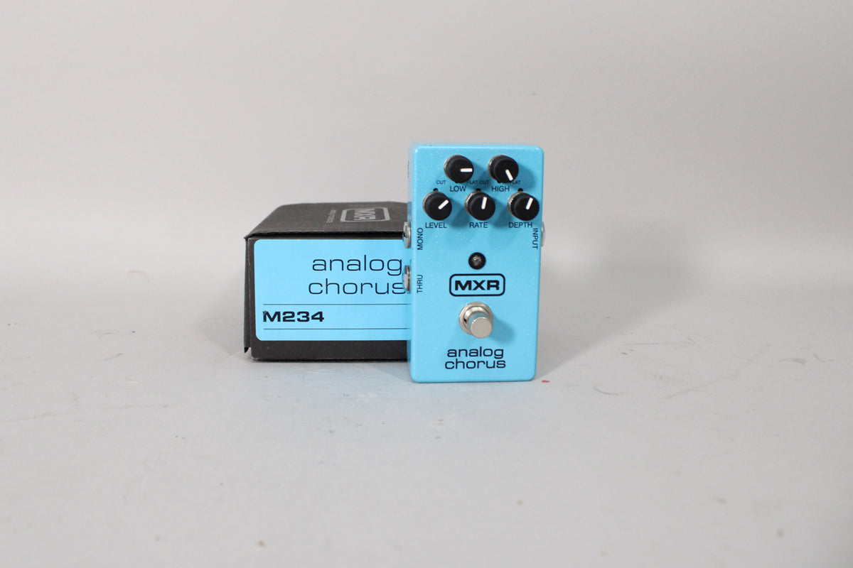 A light blue guitar pedal with five black knobs, a silver footswitch, and a black box with a matching label behind it.