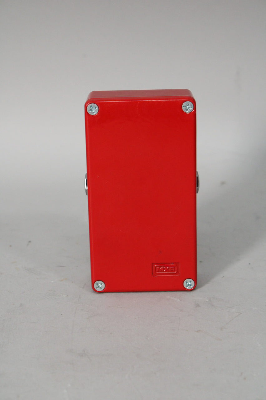 The bright red pedal is viewed from the back, showing four silver screws on the bottom plate and a small, recessed logo.