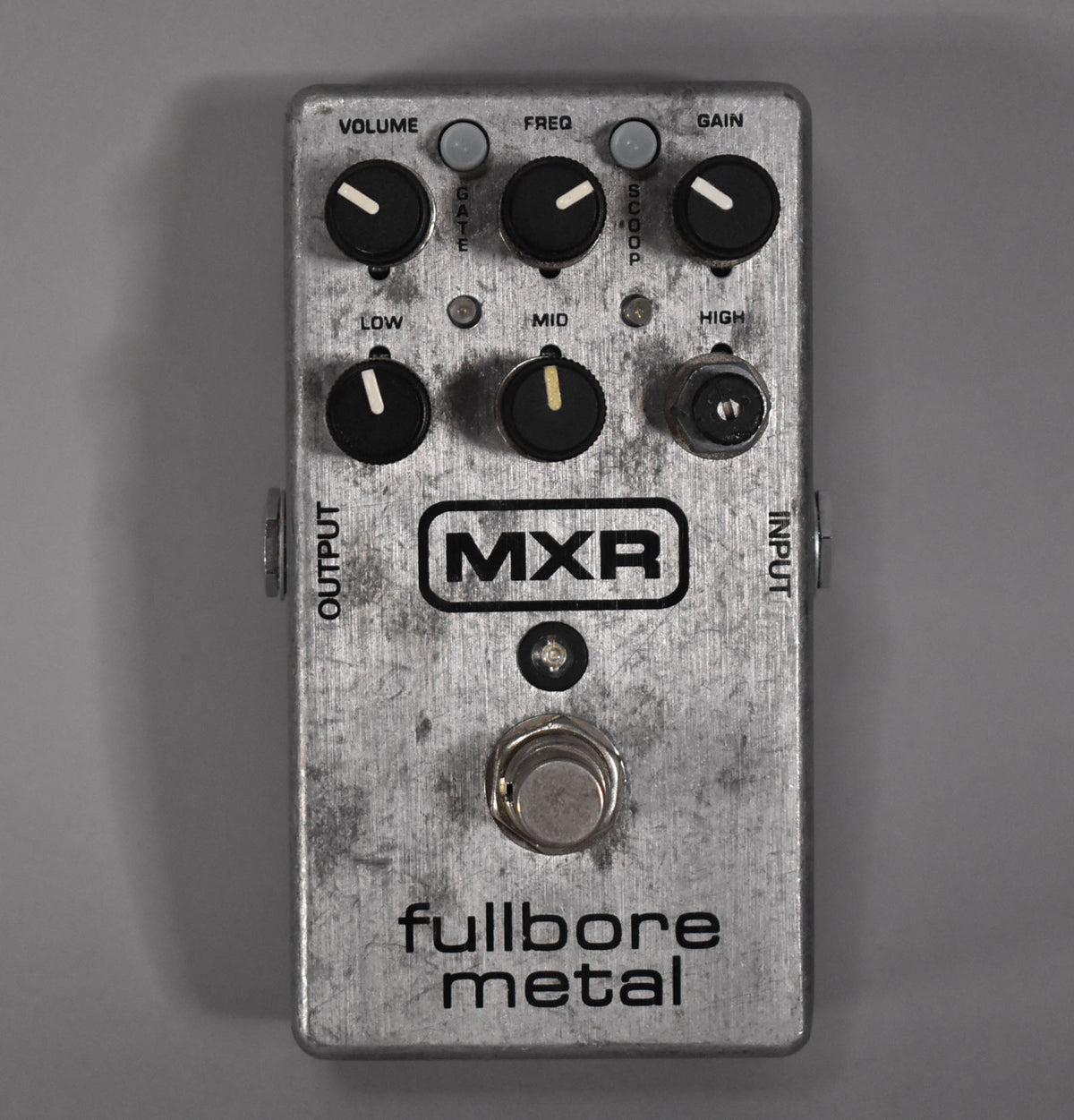 Top-down view of a brushed silver pedal with six black knobs, three small grey buttons, and a large silver footswitch.