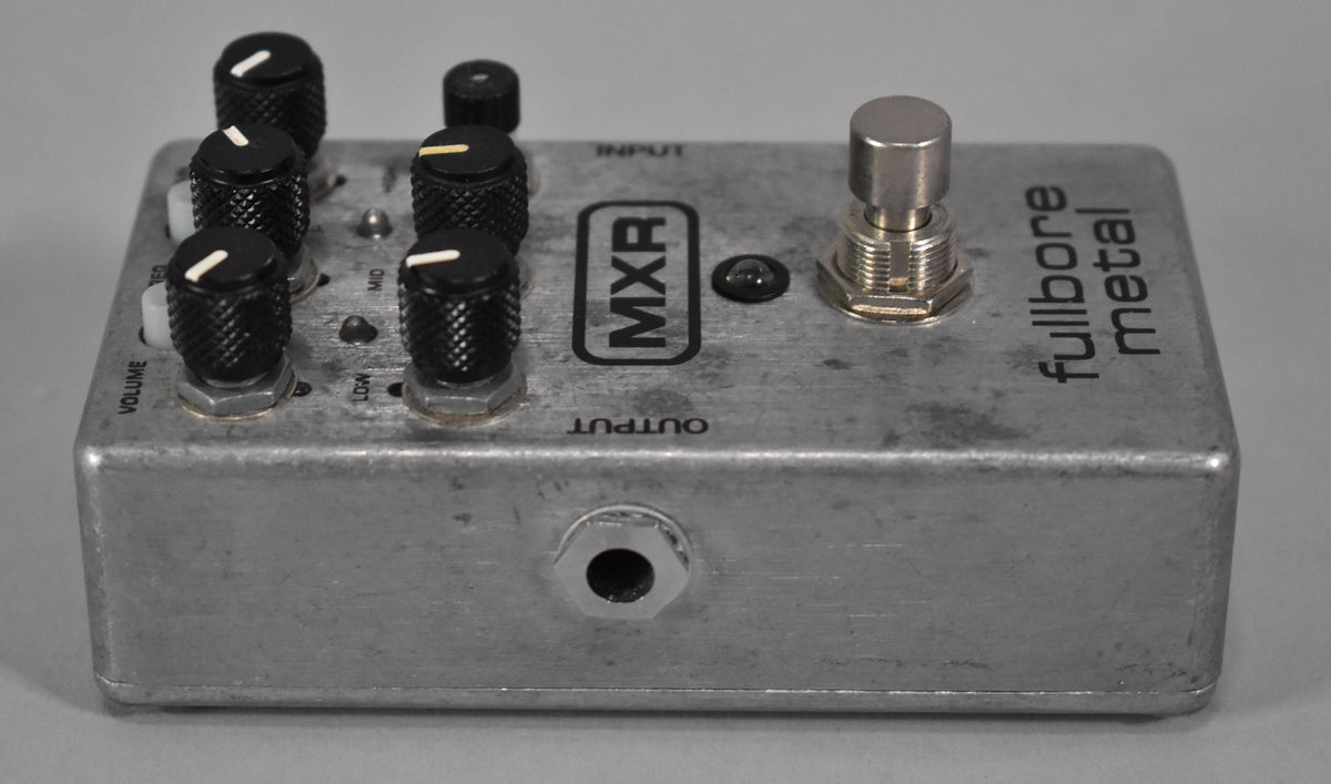 Silver metal pedal, angled from the left, showing five black knobs with white indicators, a footswitch, and an output jack.