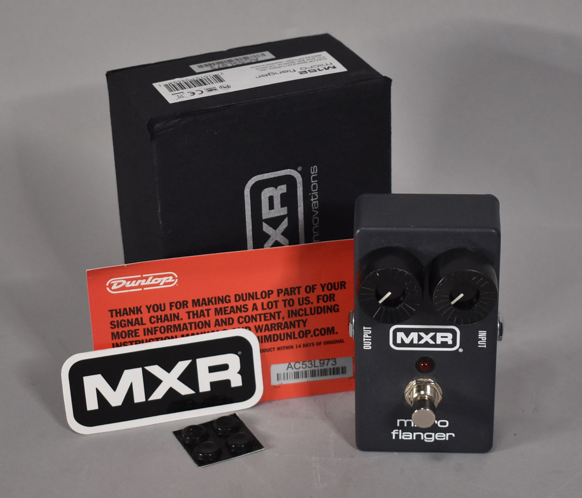 A dark gray pedal with two black knobs, a red LED, and a chrome footswitch, shown with its box and paperwork.