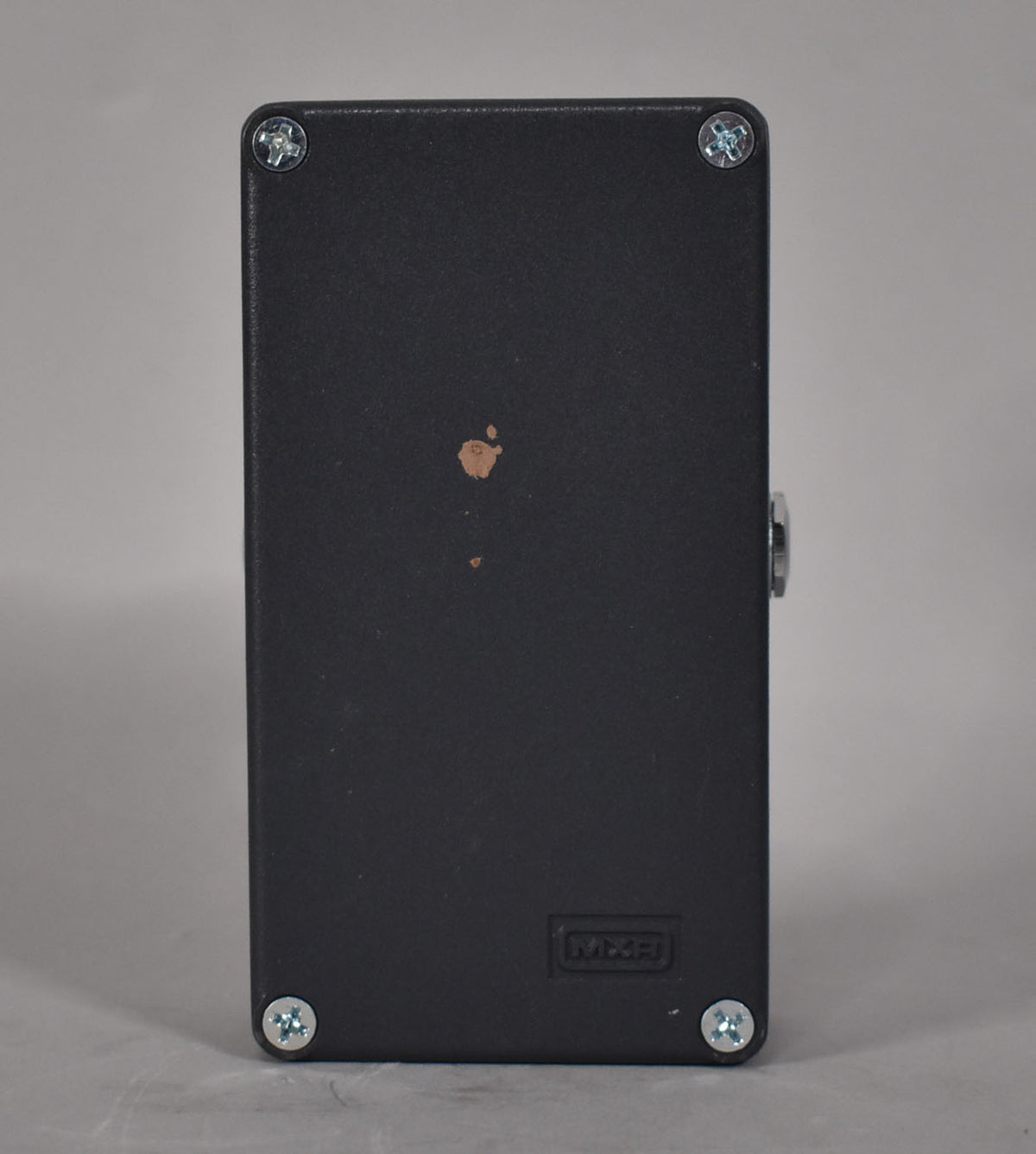 The pedal's dark gray underside is visible, secured by four silver Phillips head screws, with a small brown scuff mark near the center.