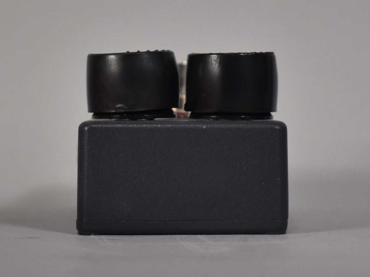 The dark gray pedal is viewed from the side, showing two black control knobs with textured tops and minor wear.