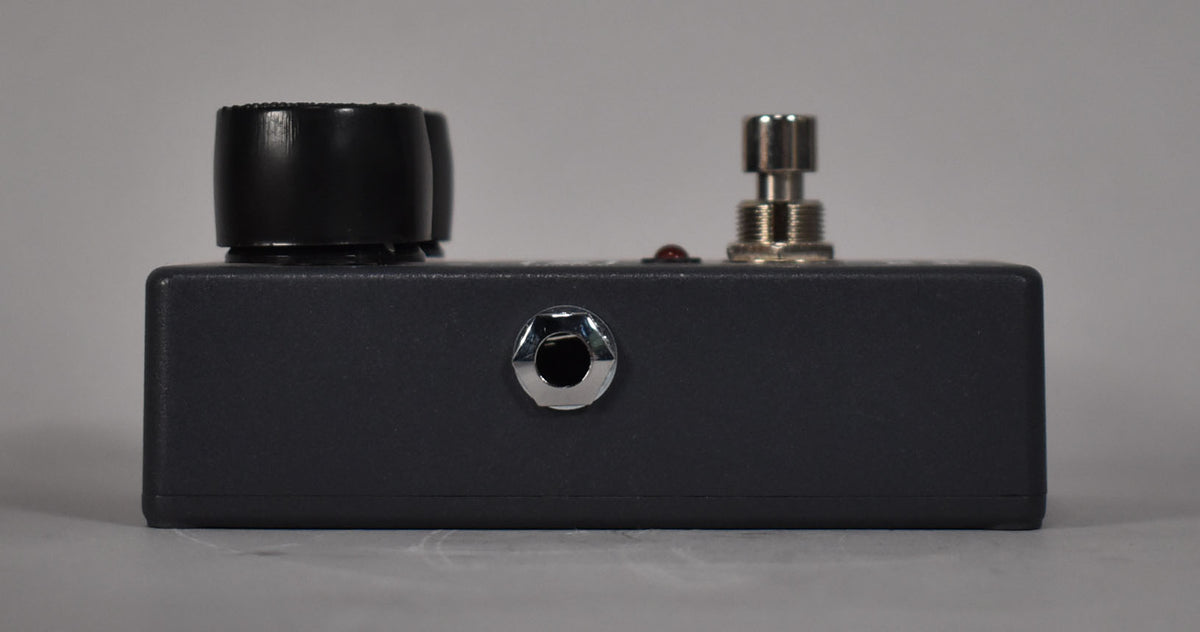 The dark gray pedal is viewed from the side, showing a silver input jack, a red LED, and a silver footswitch.
