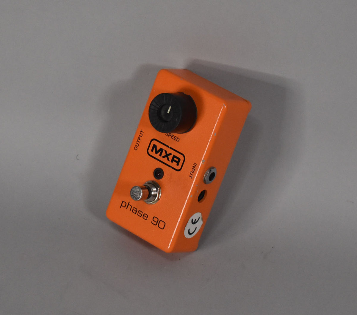 An orange guitar pedal, viewed from above and to the right, shows a single black speed knob, a footswitch, and two input jacks.