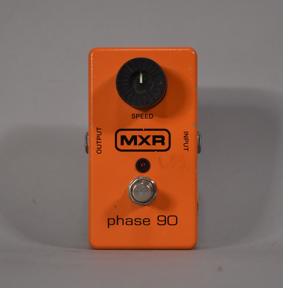Top-down view of the orange pedal, showing the black speed knob, red LED, silver footswitch, and output/input jacks.
