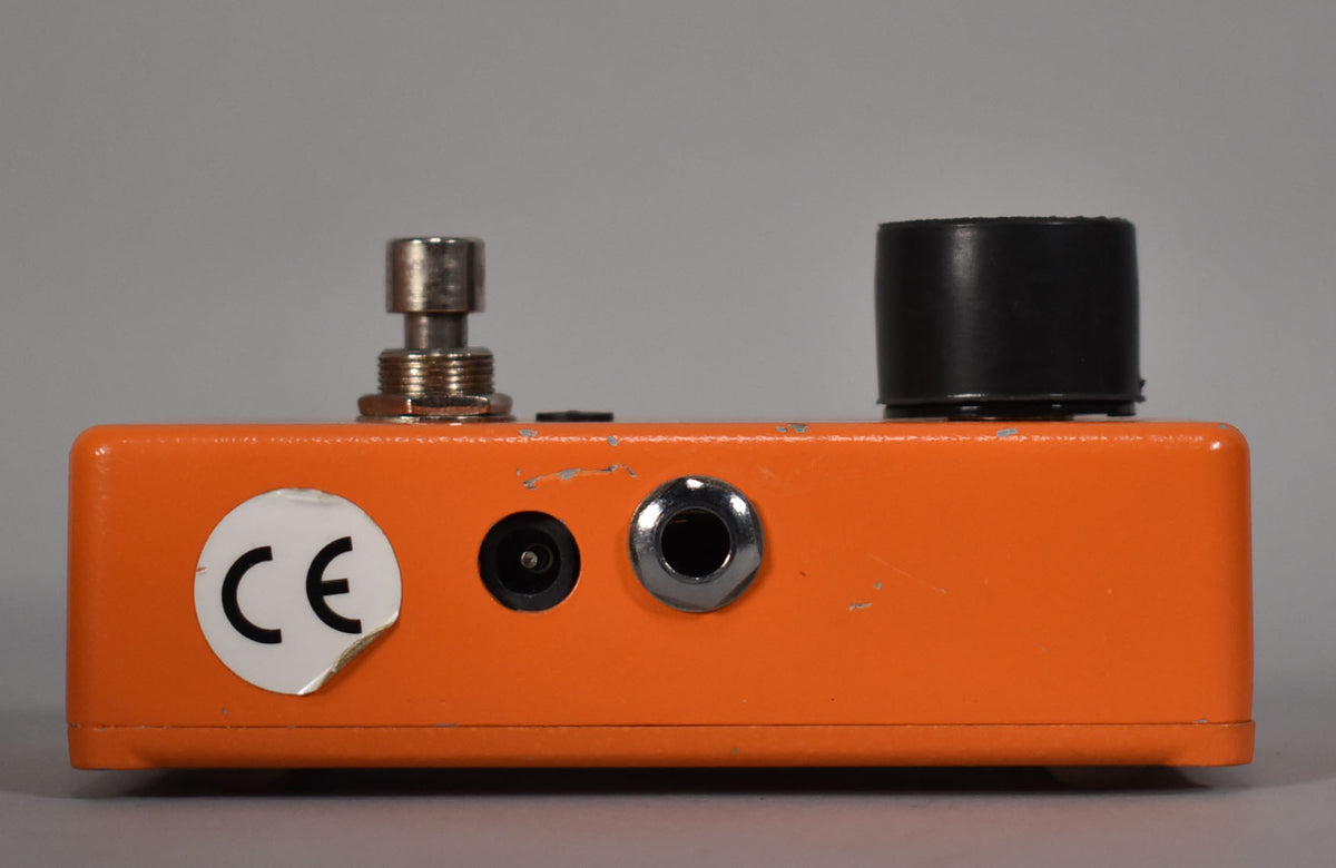The orange pedal's top edge shows a silver footswitch, a black knob, a power input, and a jack, all with visible paint chips.