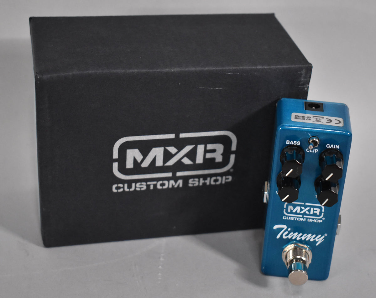 A bright blue mini pedal with four black knobs, a silver footswitch, and a black box with a white logo behind it.