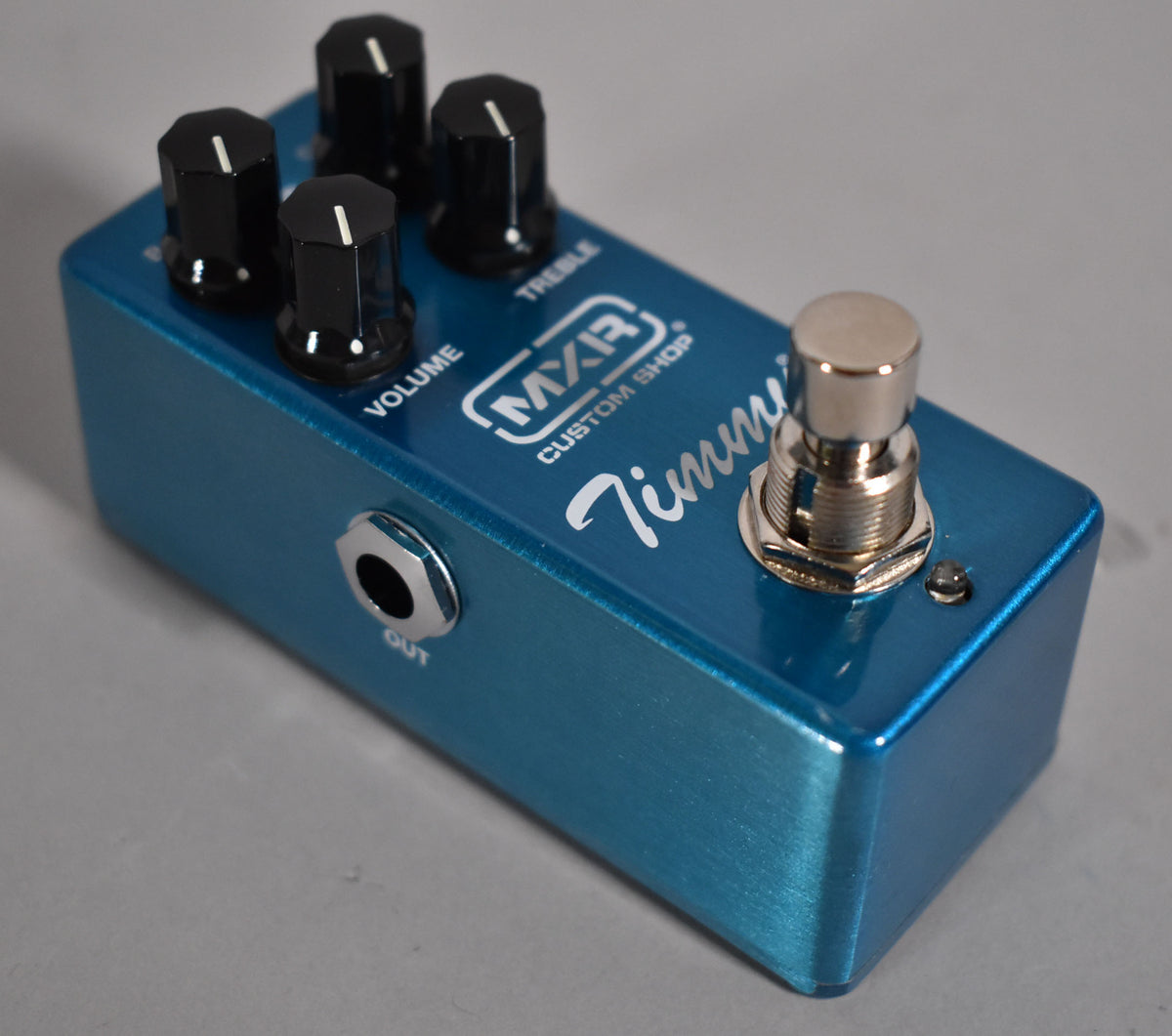 Angled view of a metallic blue pedal with four black control knobs, a chrome footswitch, and a visible "OUT" jack.