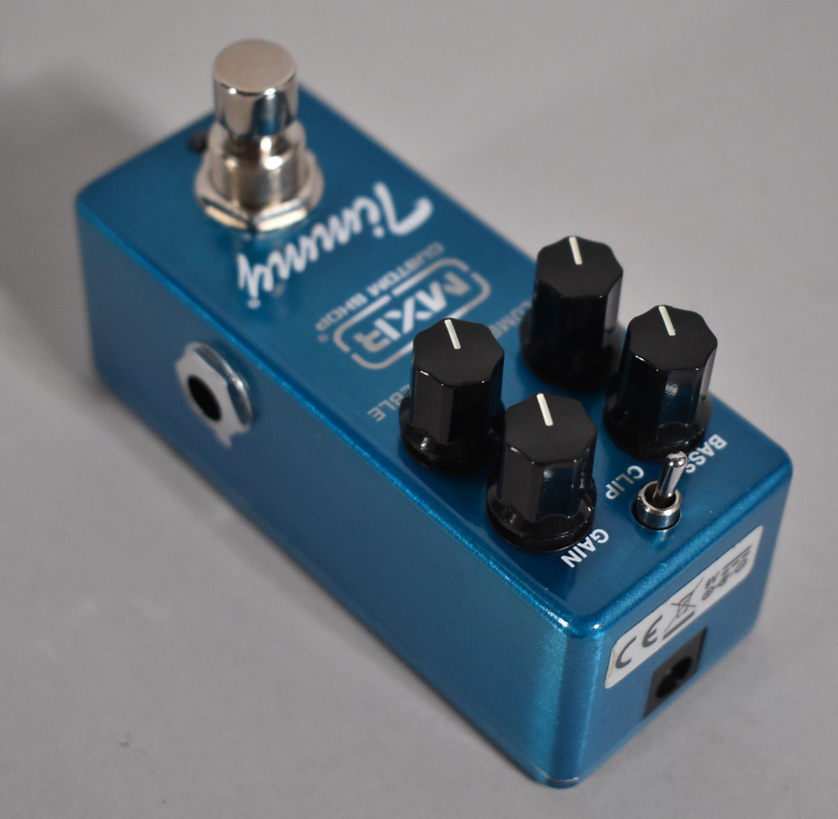 The mini pedal is bright blue with a chrome footswitch, four black control knobs, a small toggle switch, and a side input jack.