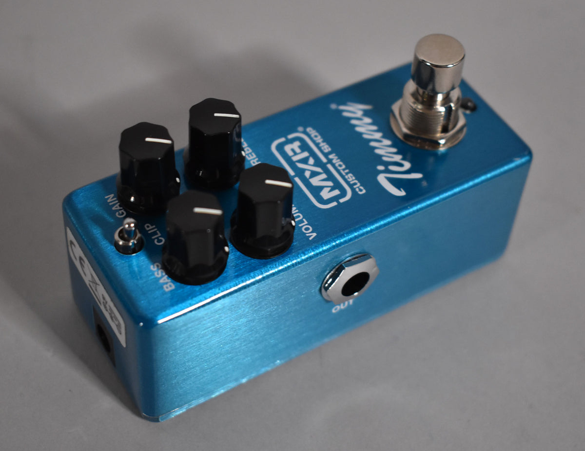 A bright blue mini pedal, angled to show the top with four black control knobs, a small toggle switch, and a footswitch.