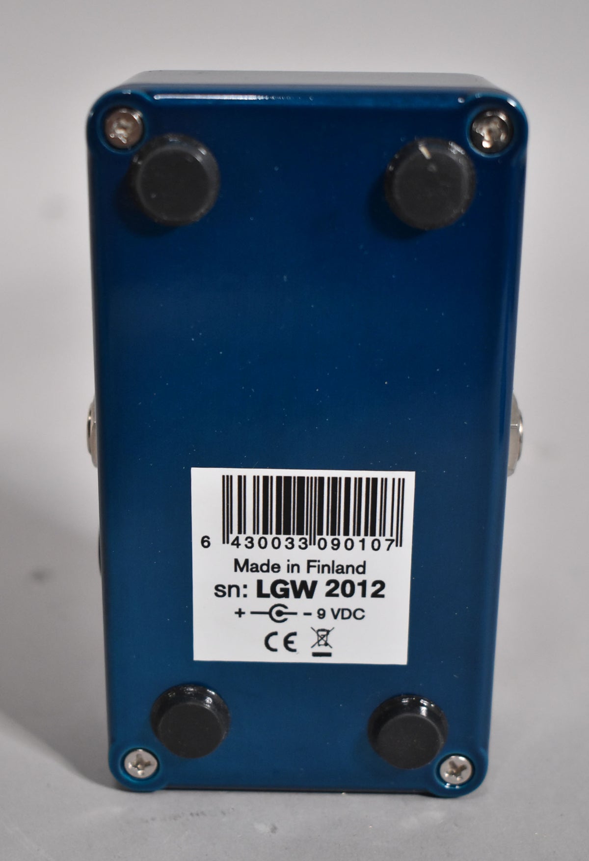 The pedal's dark blue underside, with four black rubber feet and a white sticker showing a barcode and "Made in Finland".