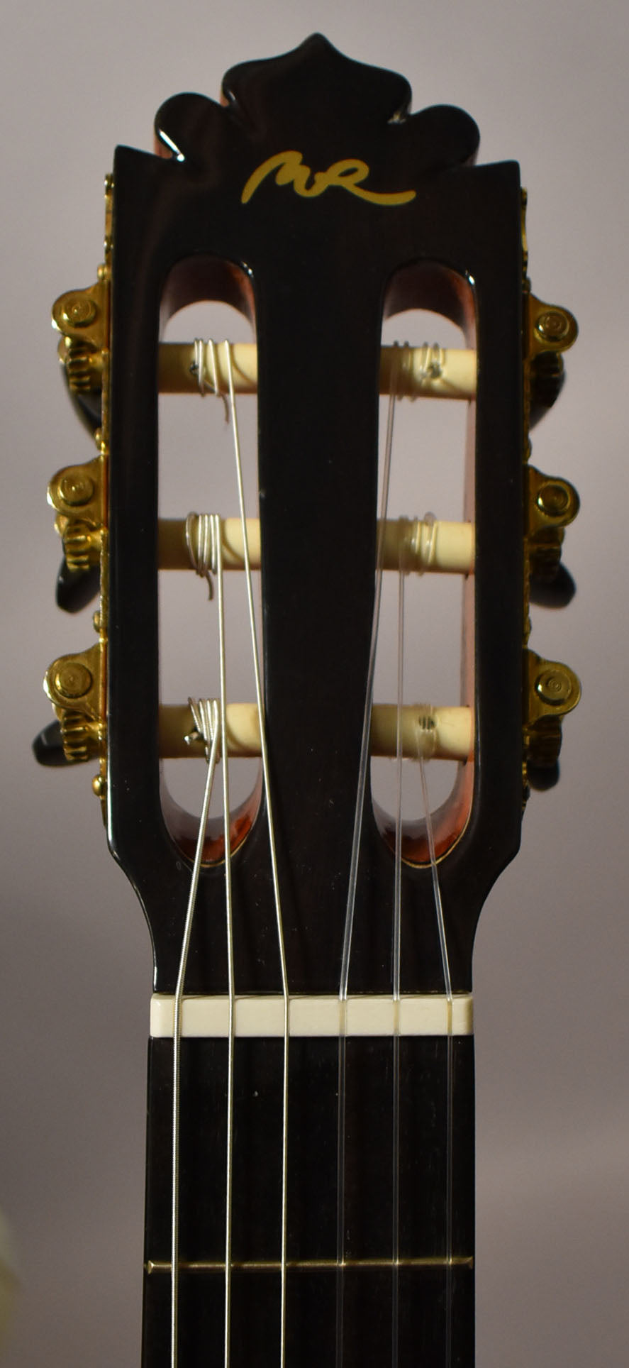 The guitar's dark headstock is framed from above the nut, showing gold tuners and a yellow script logo on the front.