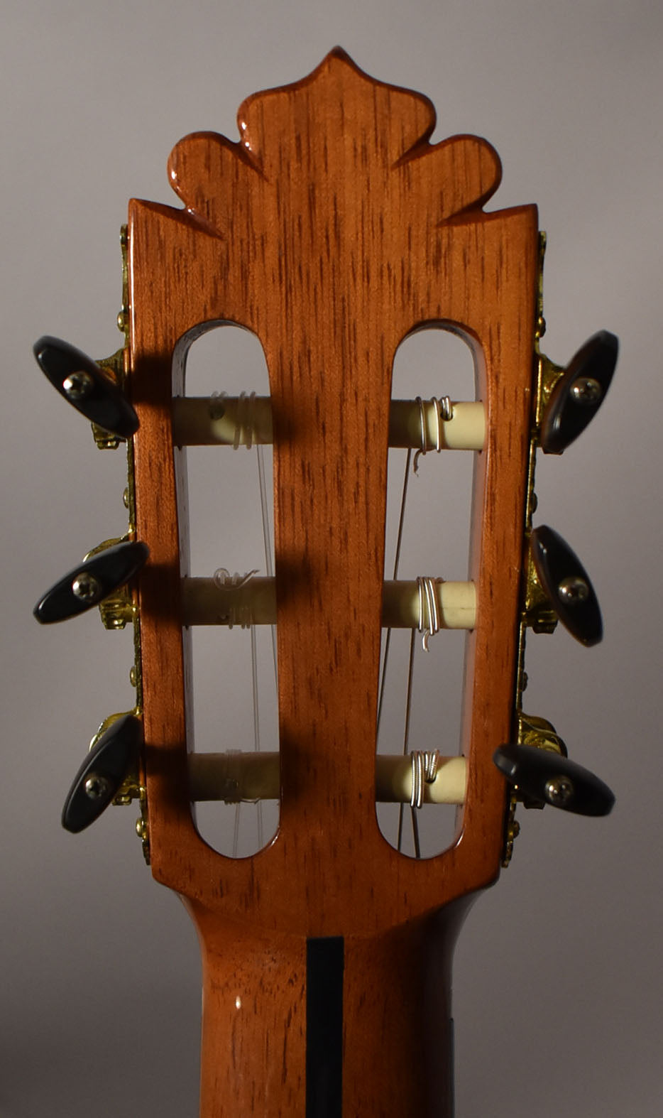 Rear view of the classical guitar headstock, showing the ornate top, open tuners with black buttons, and a dark stripe on the neck.