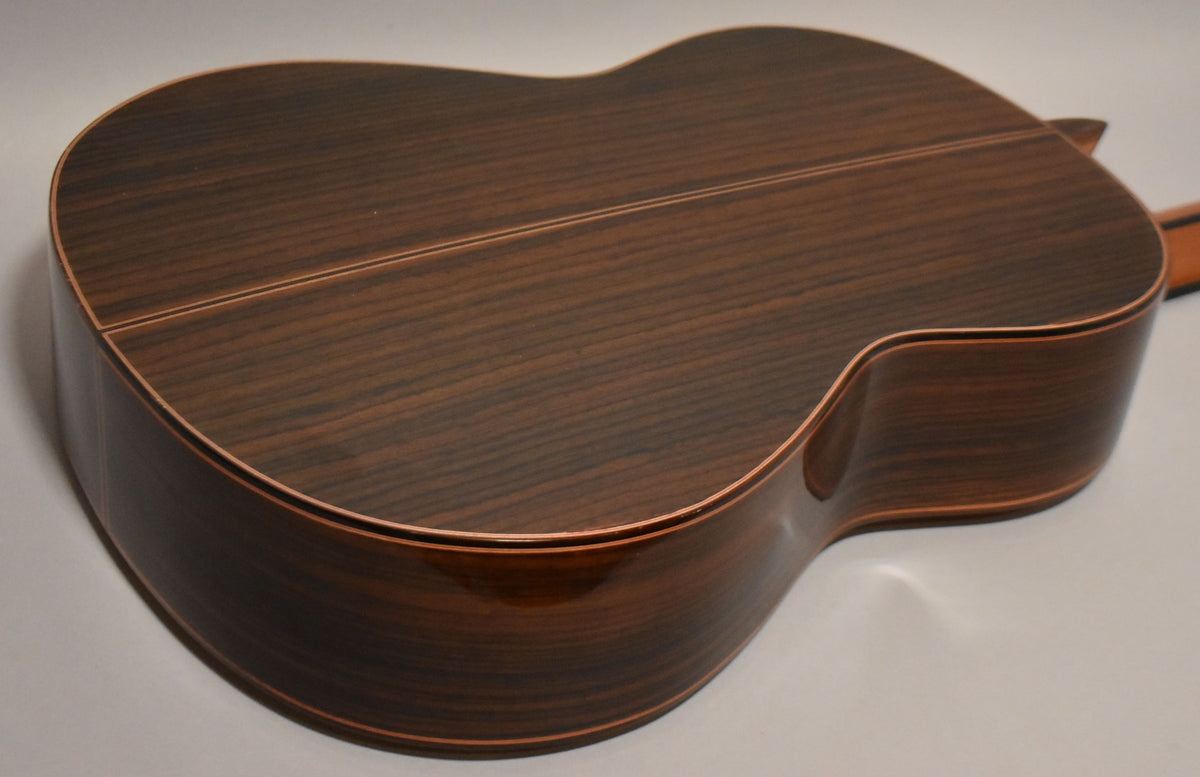 The guitar's dark brown, glossy back and sides are shown from an angle, revealing a light wood binding and a two-piece back seam.