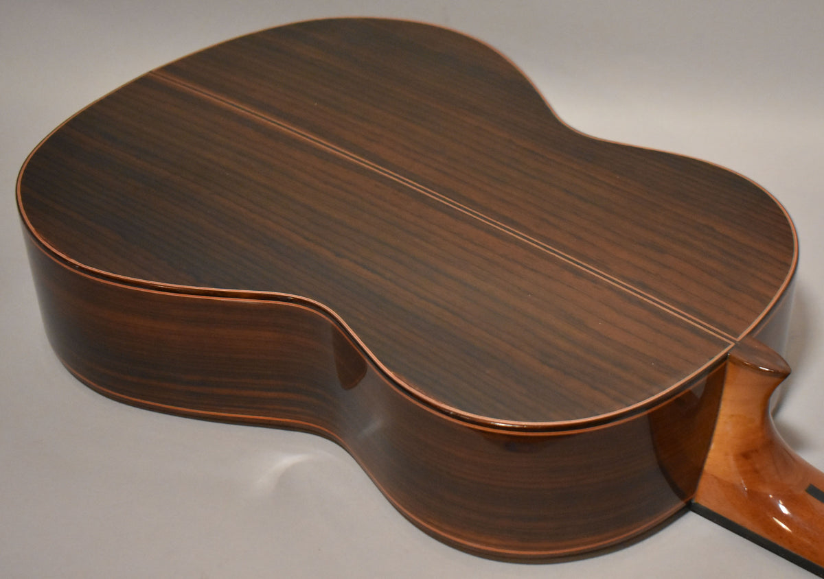 The guitar's dark brown, highly figured back and sides are shown from above, with a lighter brown neck heel visible.