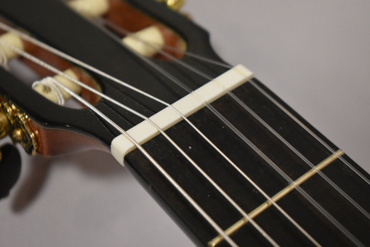 Close-up of the guitar's dark fretboard and white nut, with gold tuners and cream-colored rollers visible on the headstock.