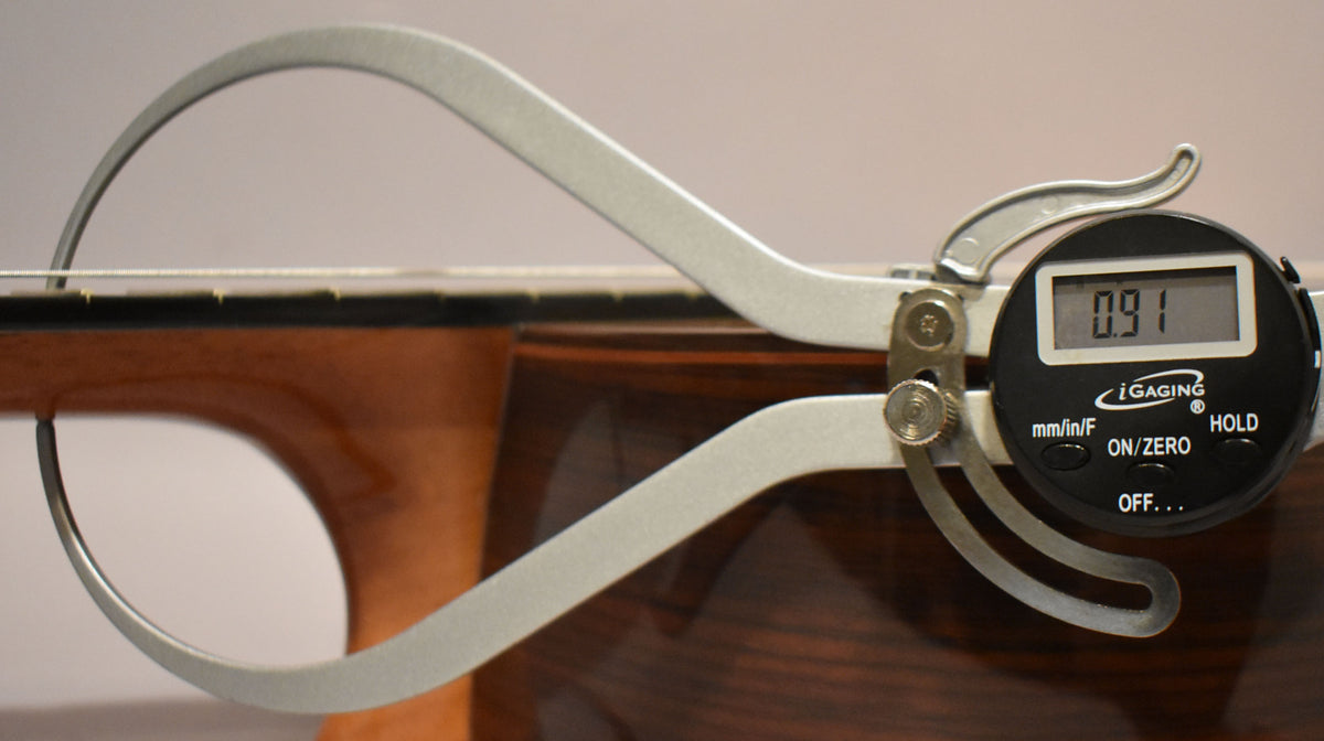 A digital caliper measures the string height at the 12th fret, showing 0.91mm above the dark rosewood fretboard.