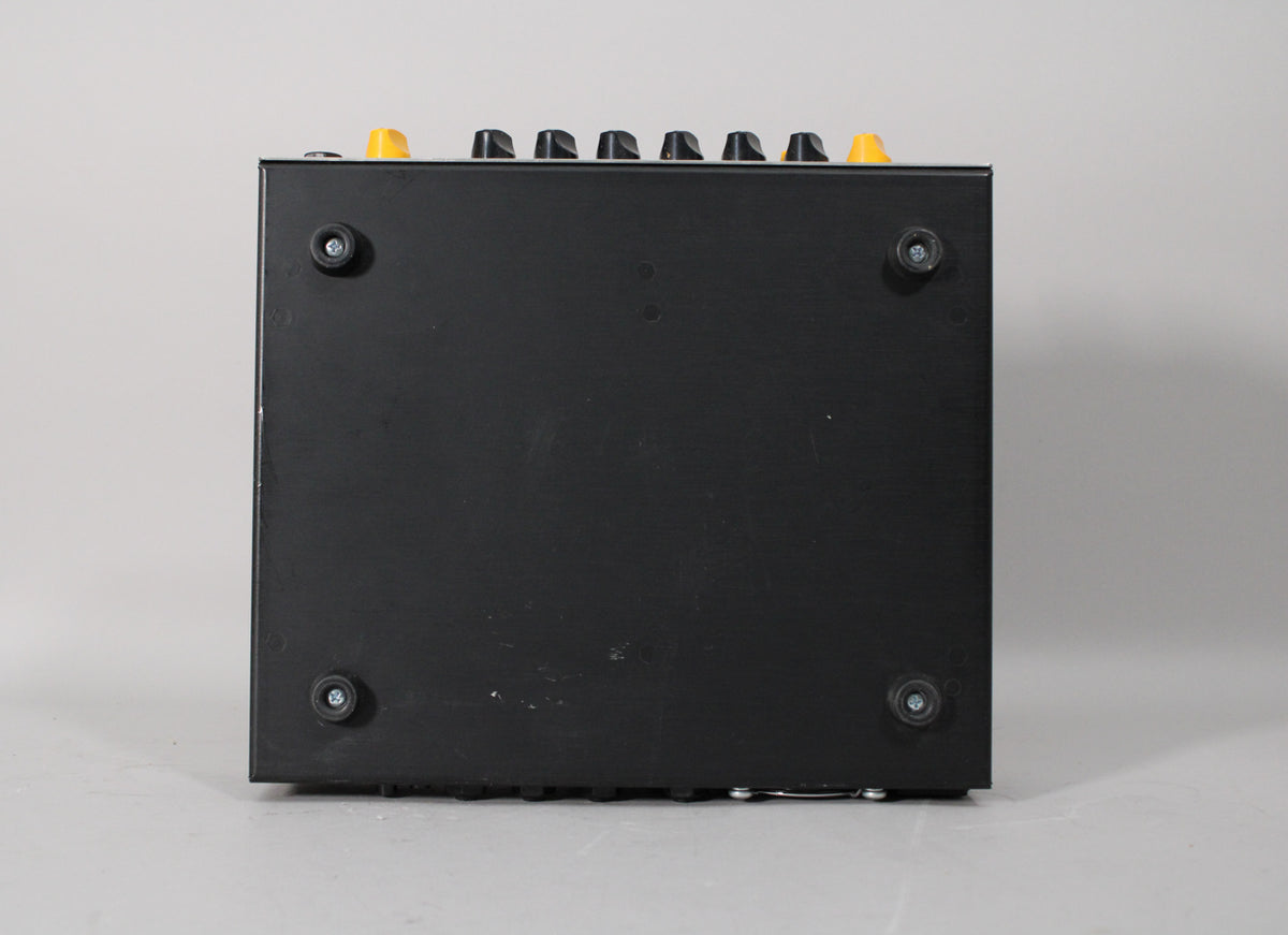 The amp head is viewed from the bottom, showing its black finish, four rubber feet, and a row of yellow and black control knobs along the top edge.