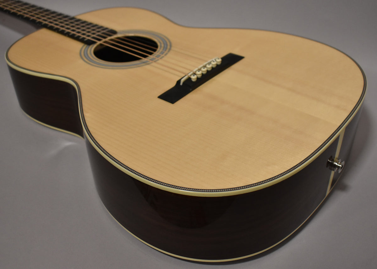 The acoustic guitar's light-colored top, dark sides, and neck are angled from the upper left, with a chrome endpin jack visible on the lower bout.