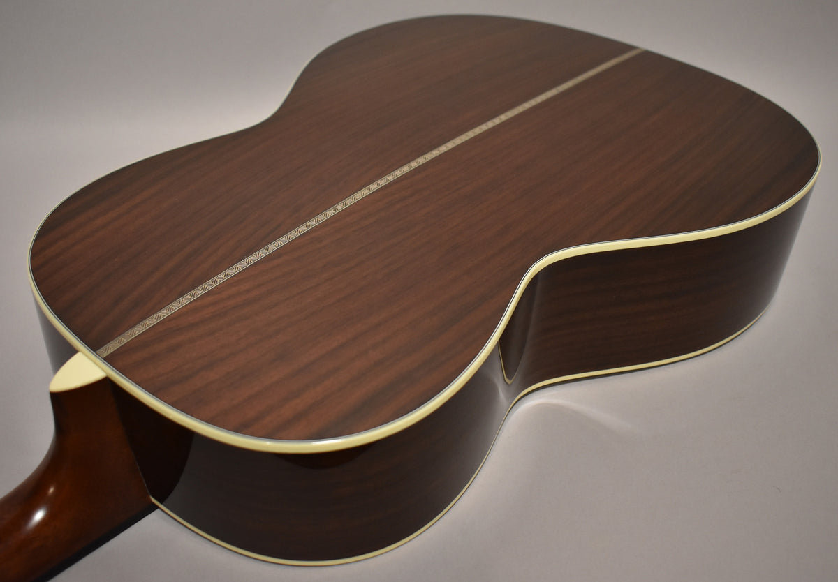 The back of the acoustic guitar, angled from the lower bout, shows dark wood grain, a light center strip, and cream binding.