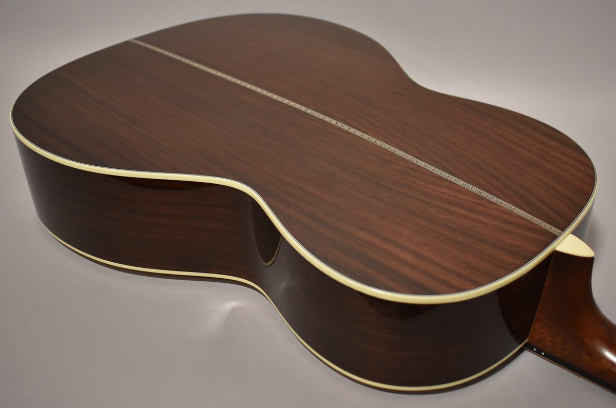 The guitar's dark brown back and sides have a glossy finish, with a decorative stripe down the center and cream binding.