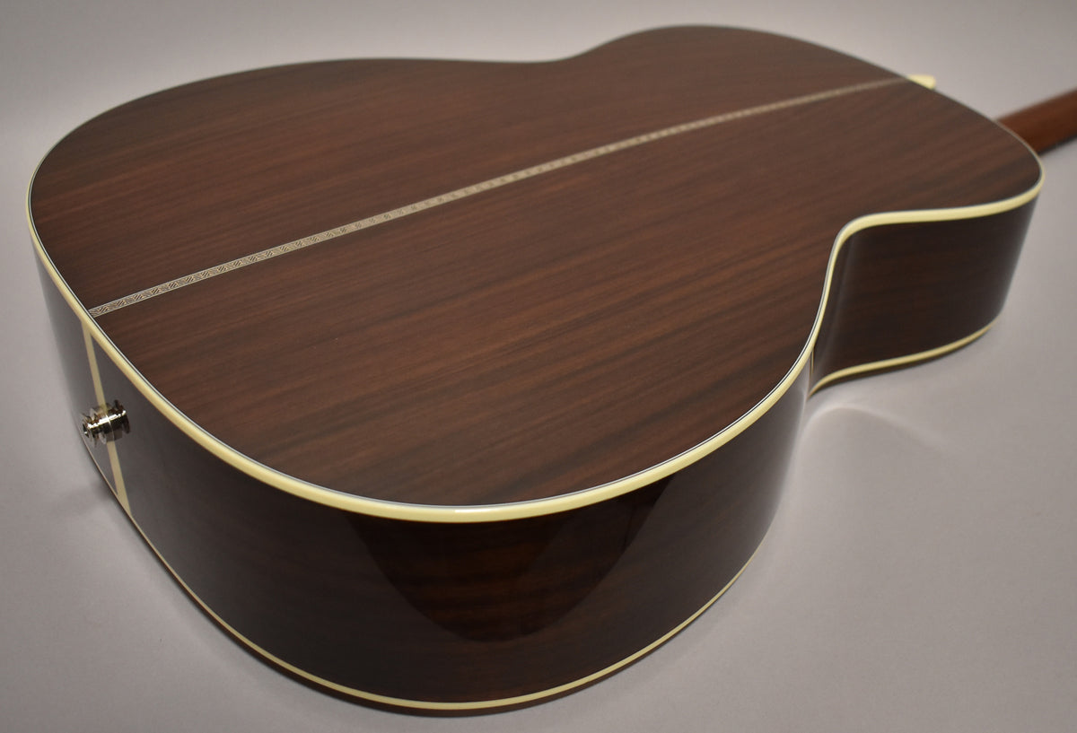 The guitar's dark brown back and sides are shown at an angle, with a light-colored binding and a chrome endpin jack visible.