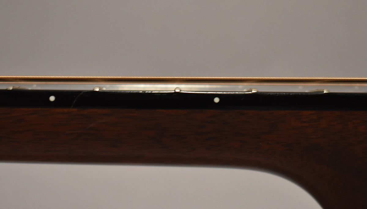A close-up of the guitar's dark brown neck and black fretboard, showing two white dot markers and a faint scratch near the nut.