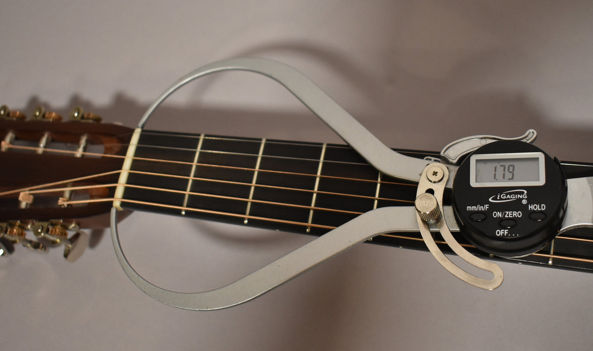 A digital caliper measures the string height at the first fret of the dark fretboard, showing "1.79" on its display.