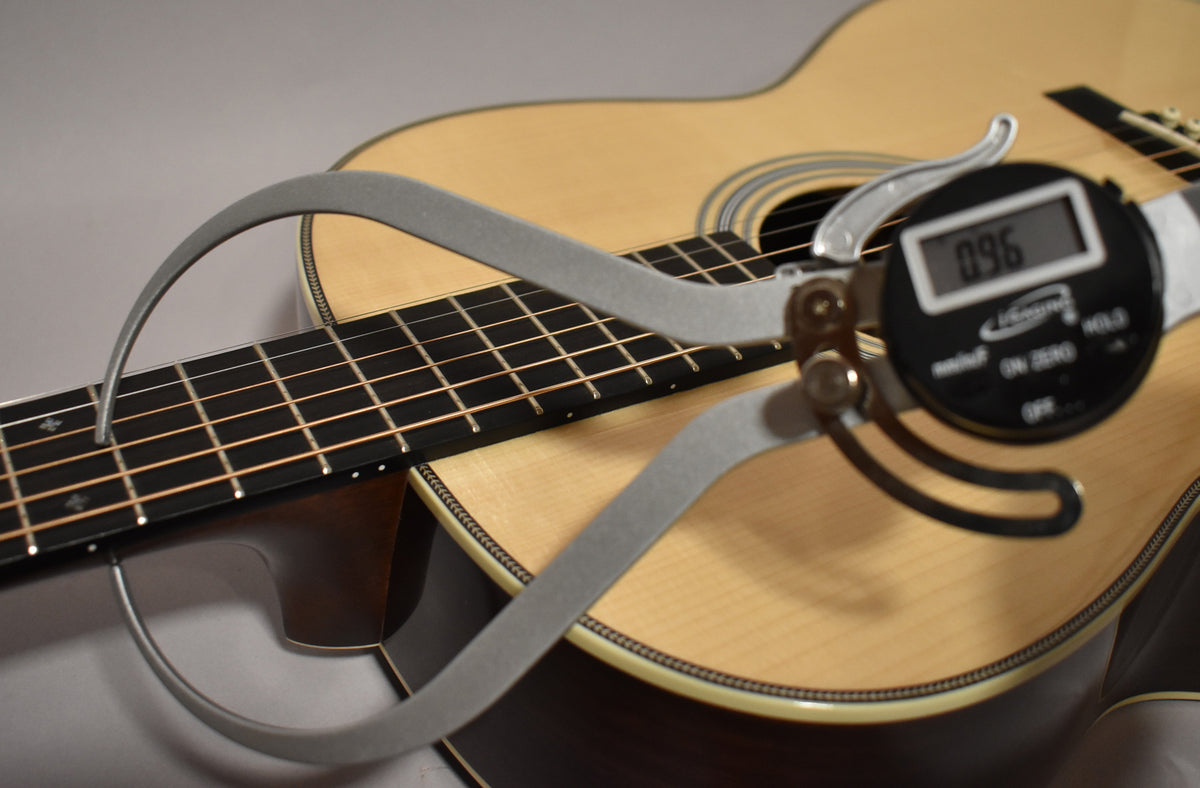 A digital caliper measures the fret height on the natural finish acoustic guitar's dark fretboard, displaying "0.96".