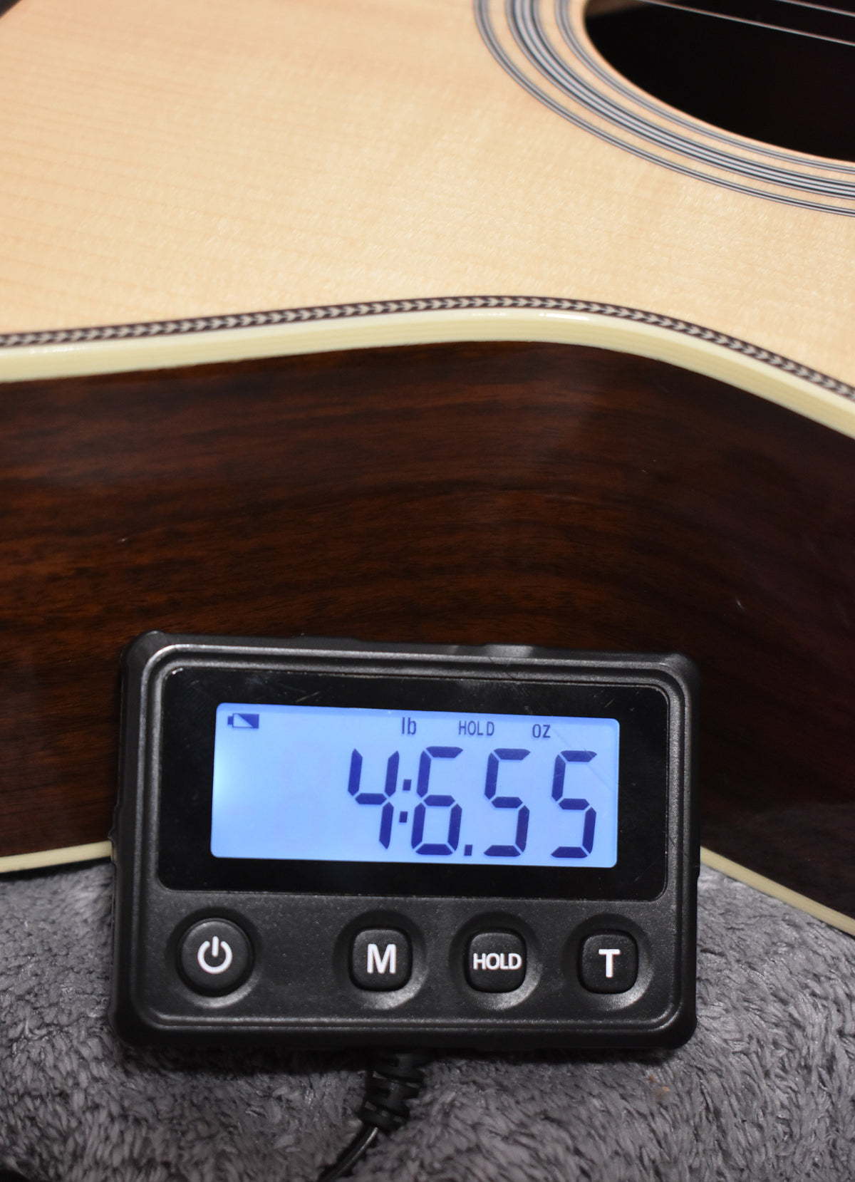 A close-up of the guitar's lower bout, with a digital scale displaying "4:6.55" (4 lbs, 6.55 oz) in the foreground.
